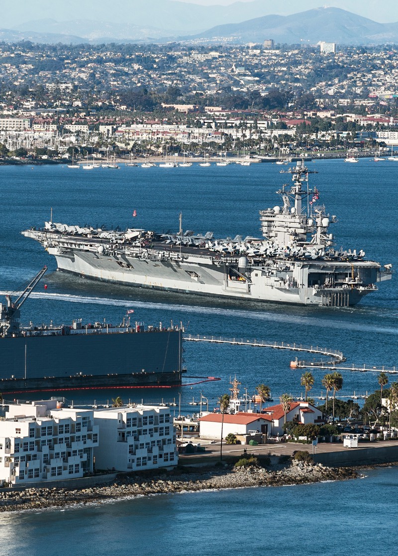 Aircraft carrier in the San Diego Bay with houses and buildings visible along the coastline